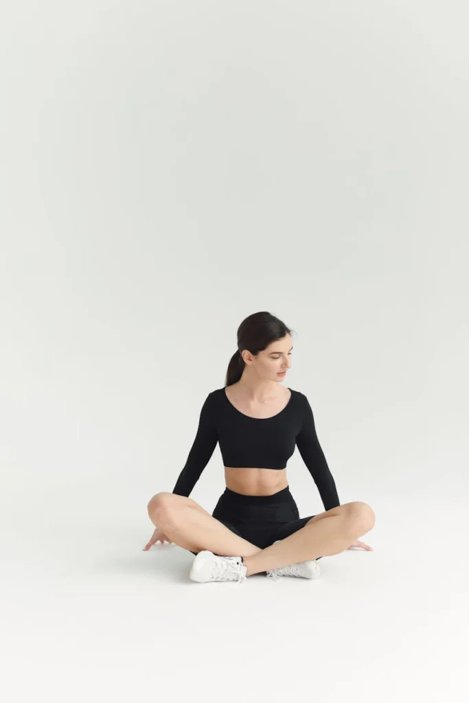 Fit woman in studio setting wearing black athletic wear, sitting cross-legged. Great for fitness or lifestyle projects.