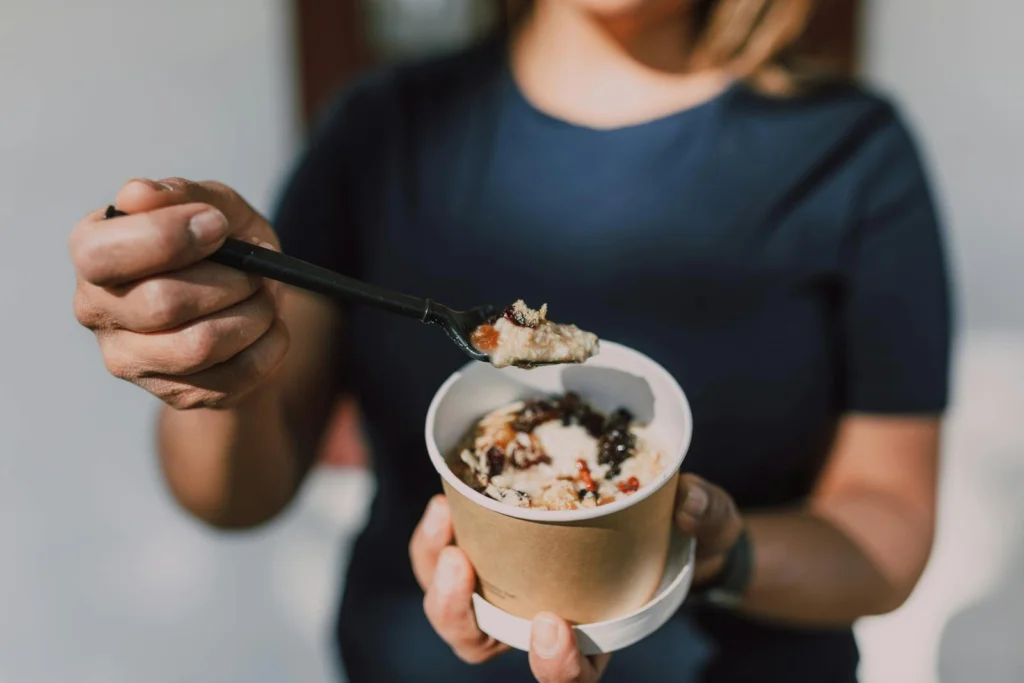 Close-up of a person holding a bowl of vegan oatmeal topped with fruits.
