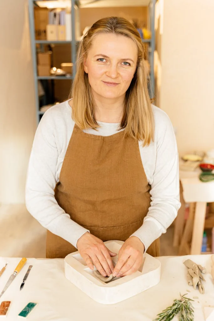 Woman in apron molds clay on a work table, showcasing craftsmanship indoors.