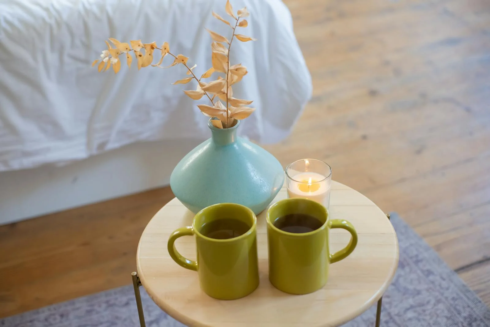 Two green mugs on a table with a vase and candle, evoking a cozy indoor atmosphere.
