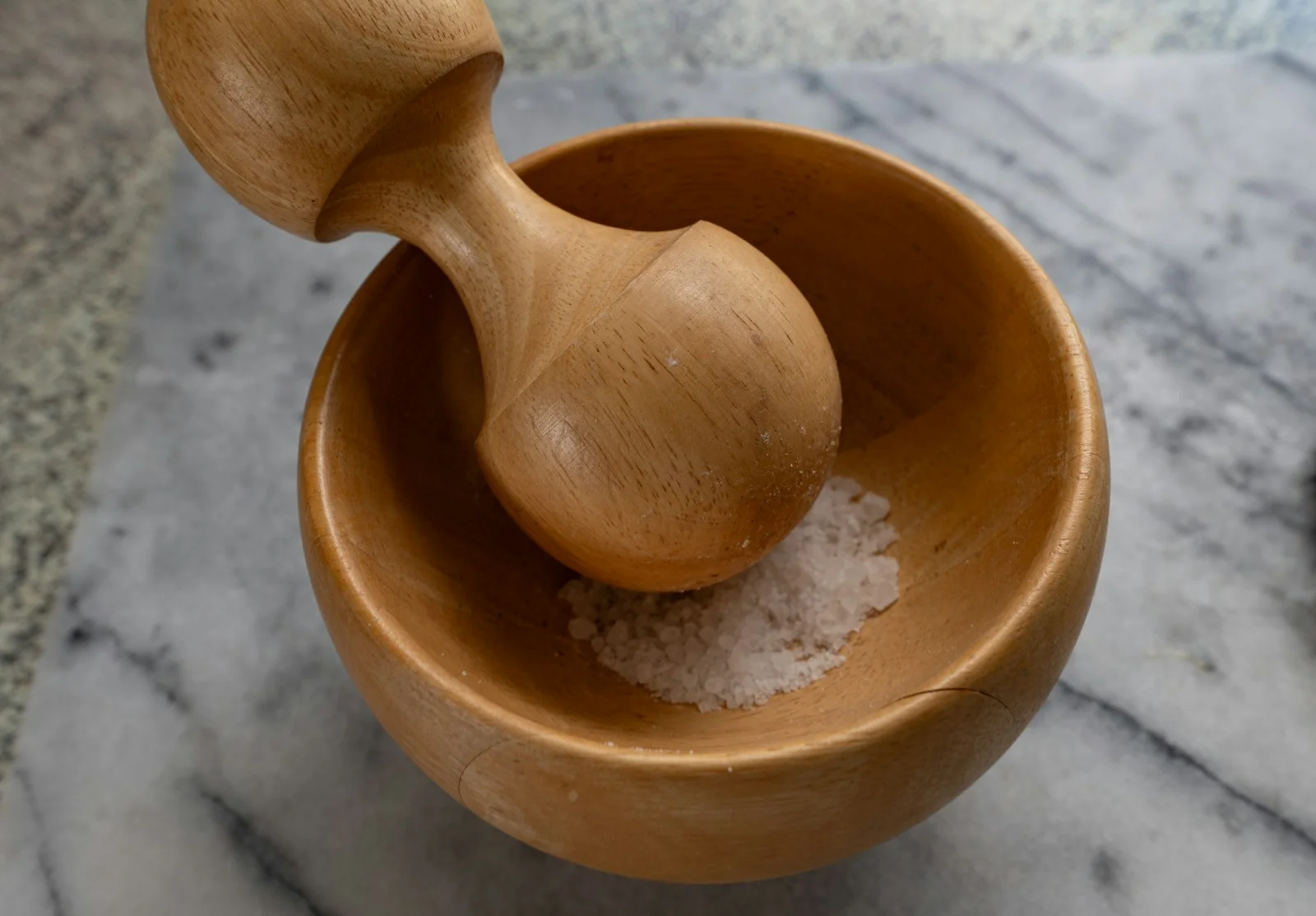 A wooden mortar and pestle with salt.