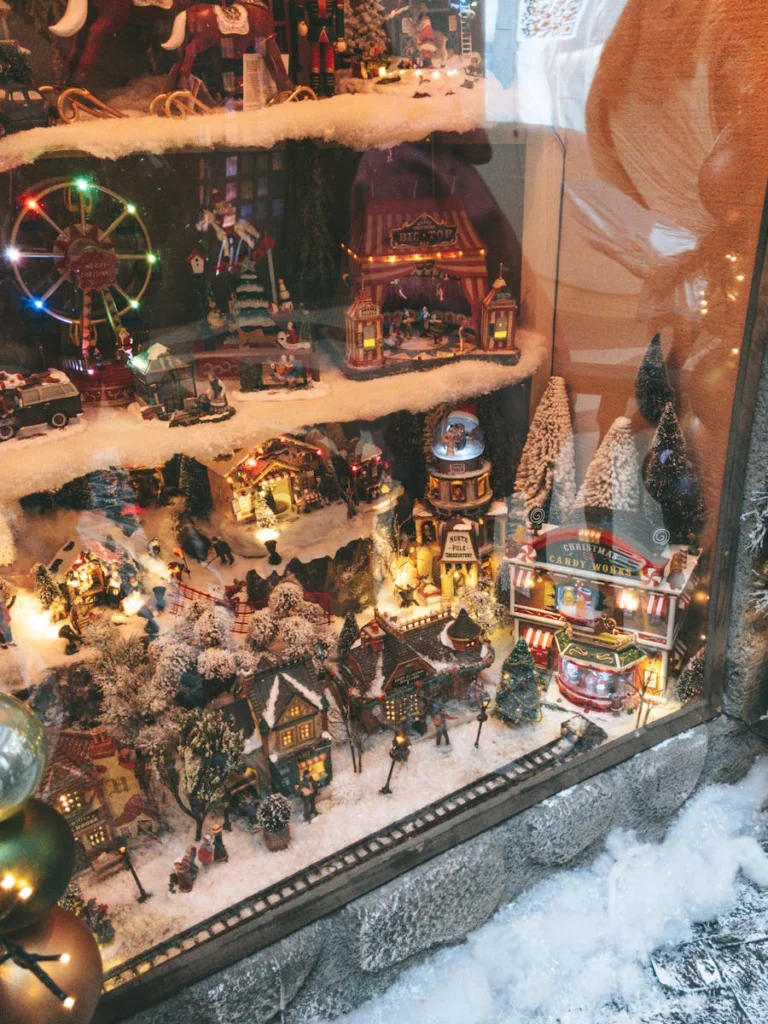 Charming Christmas village display in a store window with festive decorations and miniatures.