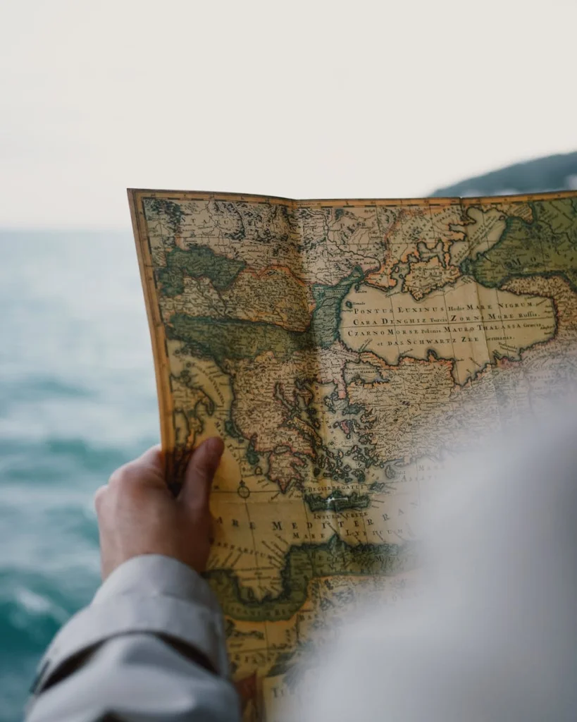 A person holding a vintage map by the sea, possibly Turkey.
