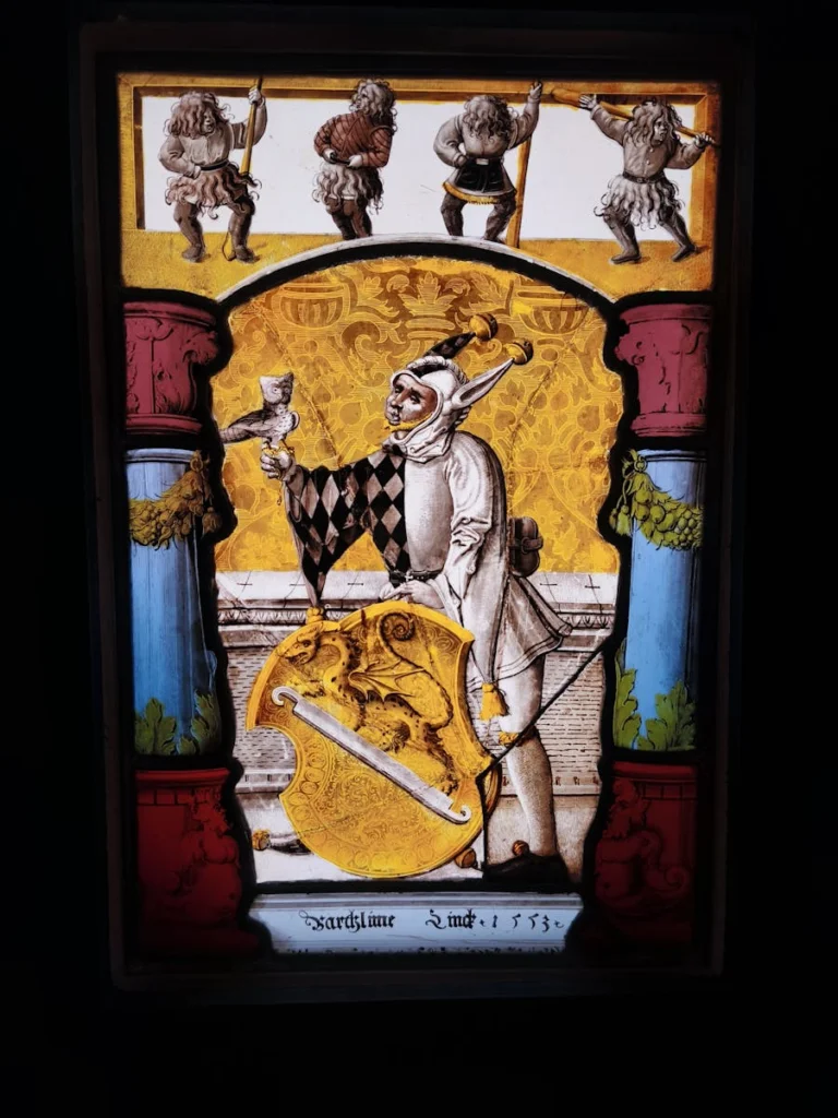 Stained glass window depicting a jester with heraldic shield.