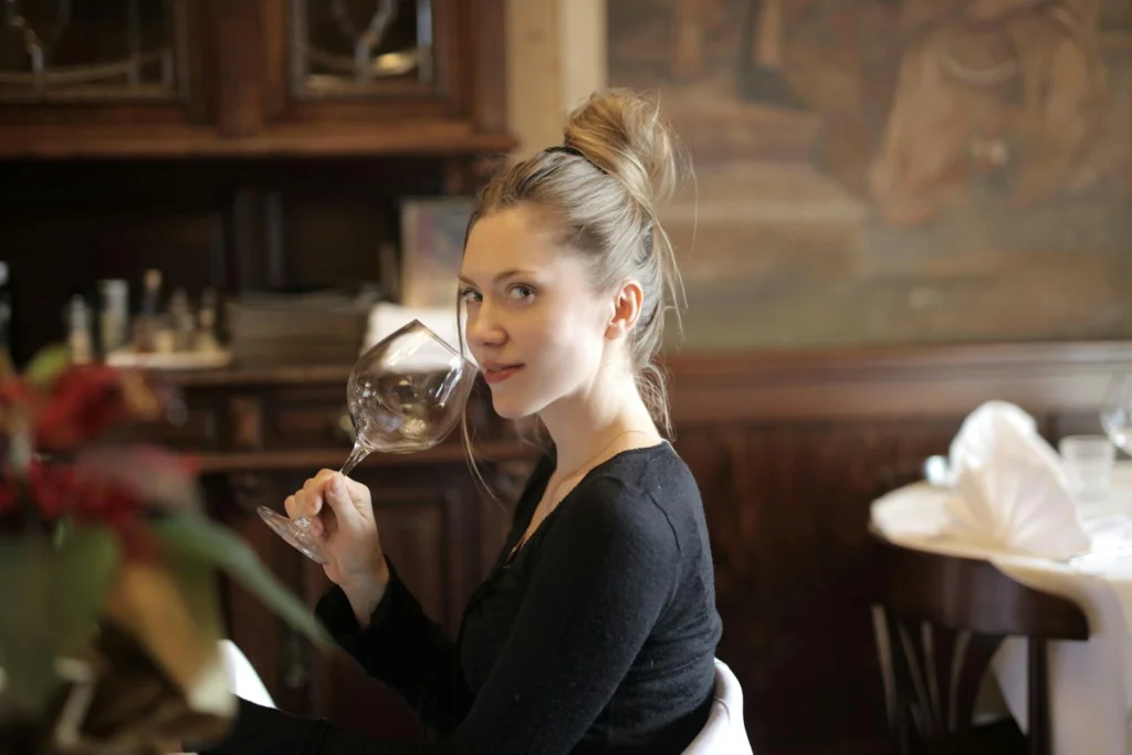A woman enjoys a glass of red wine in an elegant indoor restaurant setting.