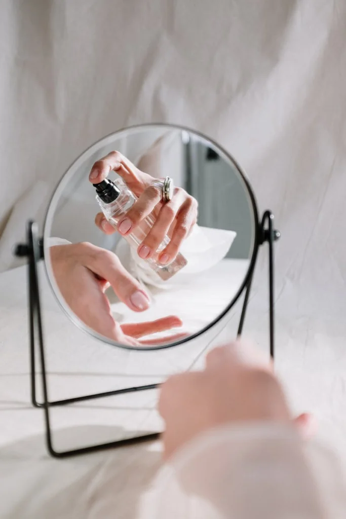 A graceful hand holding a perfume bottle reflected in a mirror, creating an elegant scene.