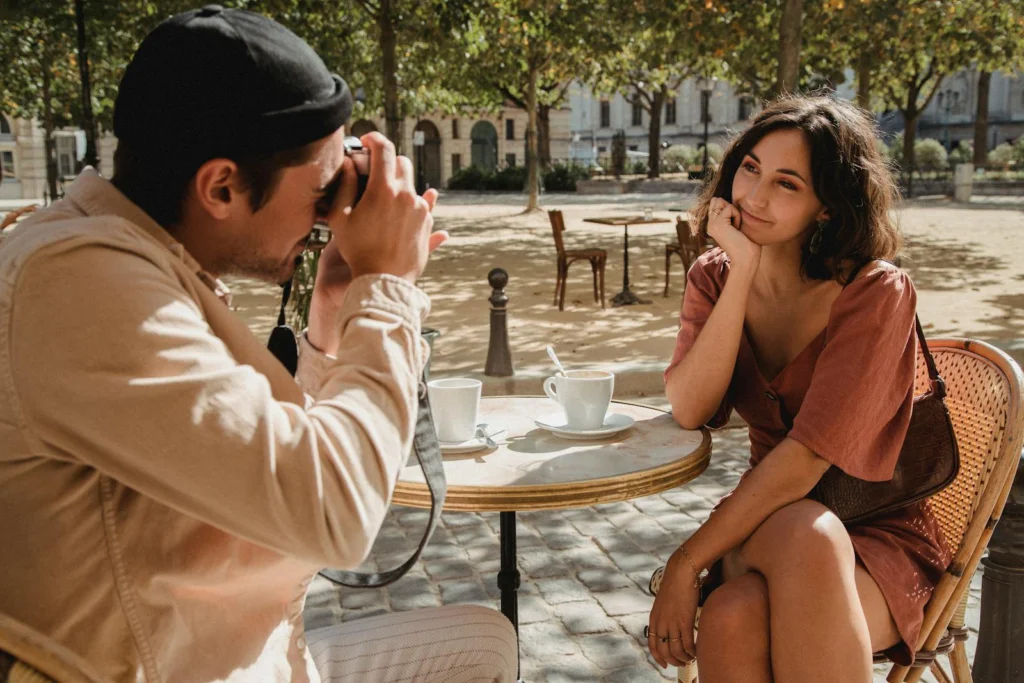 A man photographs a smiling woman at an outdoor café, capturing candid moments.
