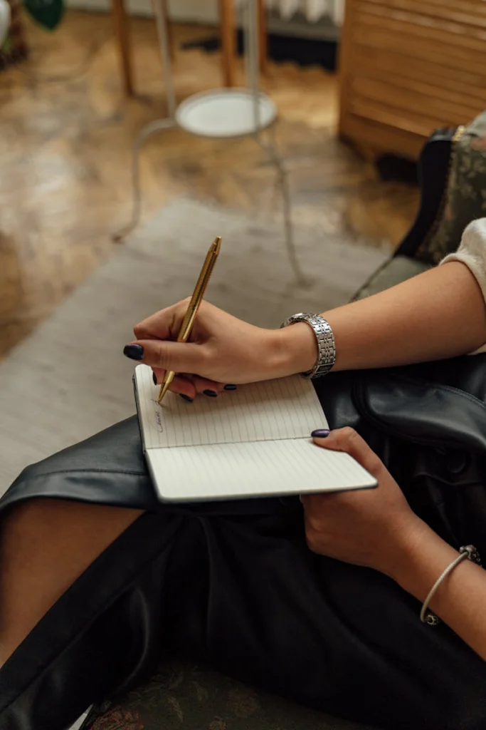 Close-up of hands writing in a notebook with a pen, indoors on a cozy setting.