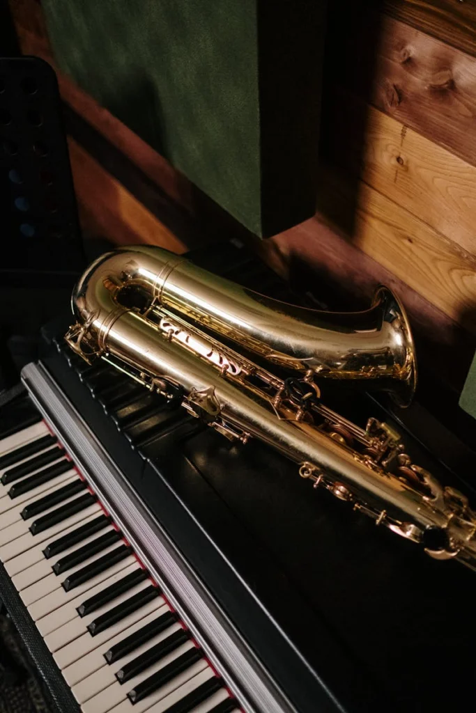 A gold saxophone resting on a black piano in a cozy, wooden music studio.