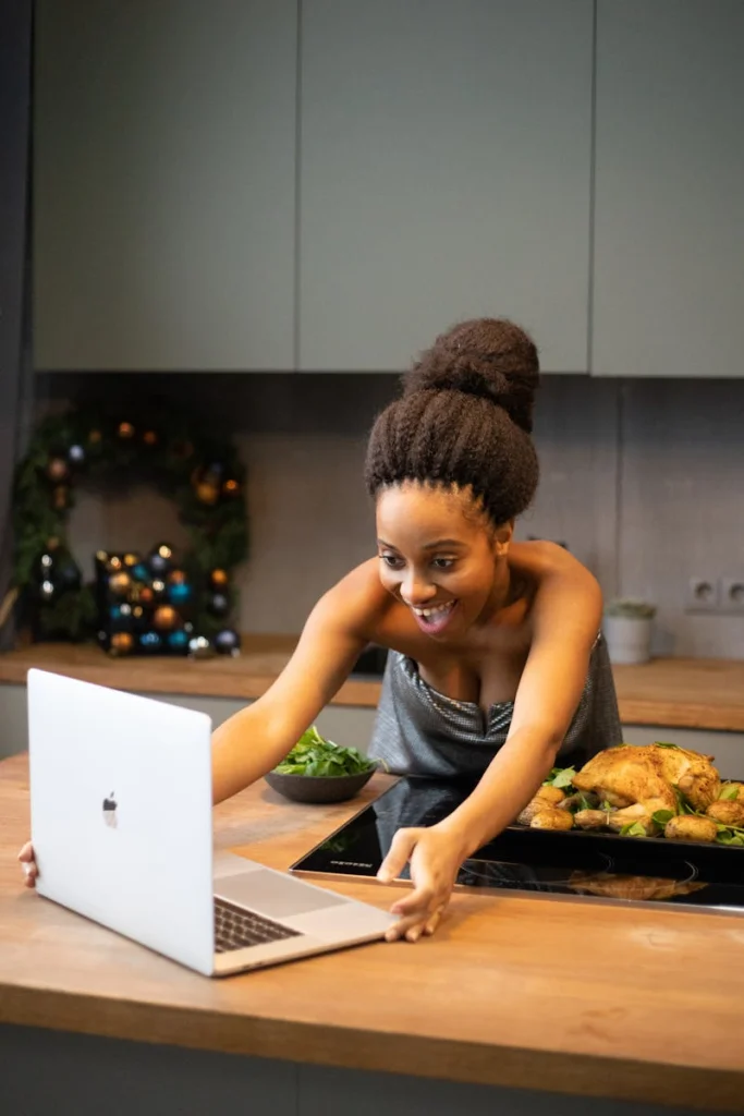 Cheerful woman video calling from kitchen with cooked dish, enjoying online interaction.