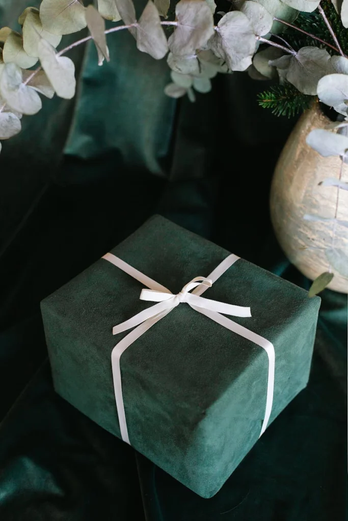 A luxurious green gift box wrapped in white ribbon, set against a lush velvet background.