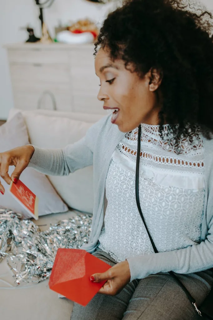 Smiling woman reads holiday cards at a festive indoor gathering.
