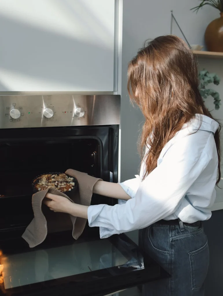 Woman placing a freshly baked pie into the oven in a sunny modern kitchen.