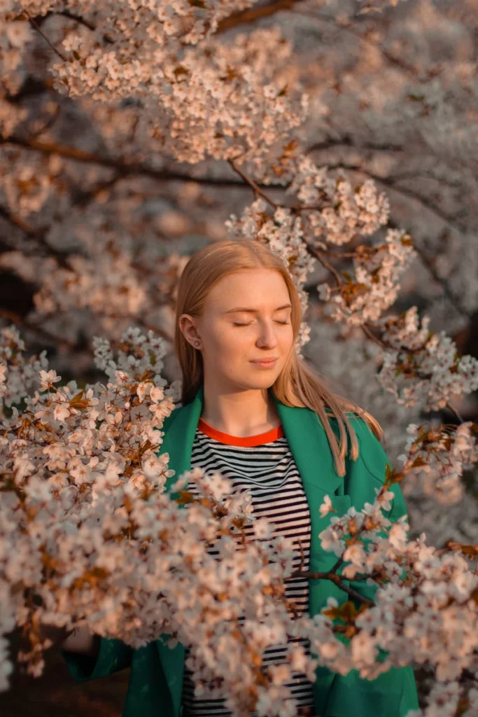 Woman peacefully surrounded by blossoming cherry blossoms in a serene spring setting.