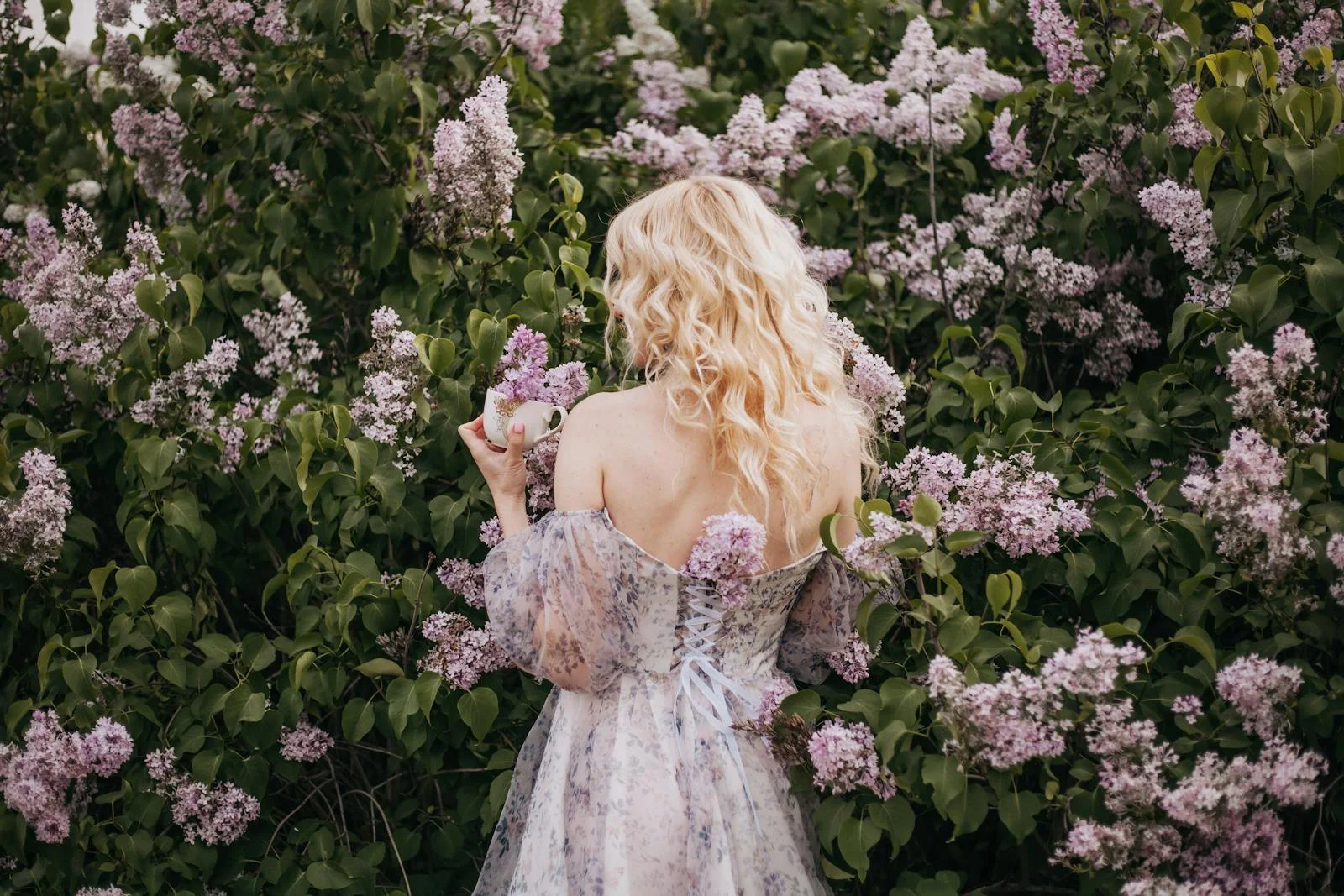 A woman in a floral dress stands amongst blooming lilacs, capturing spring's essence.