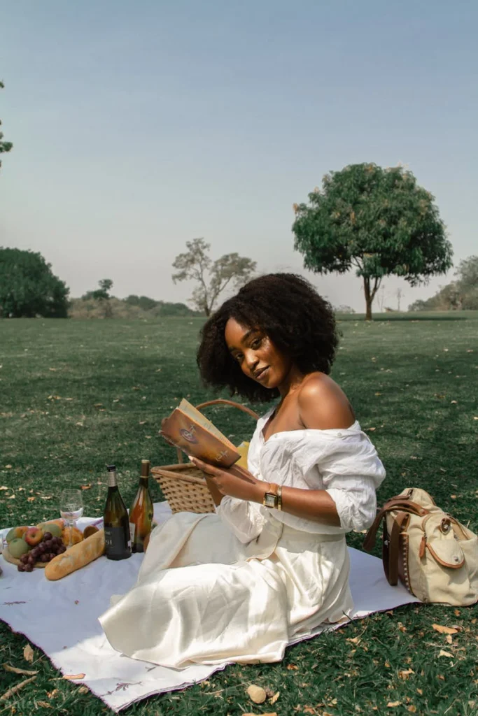 A woman enjoys a serene picnic in a sunny park setting.