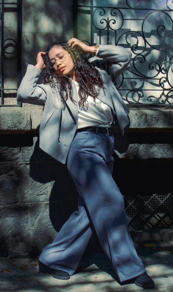 Stylish woman in grey suit posing by ornate railing in sunlight.