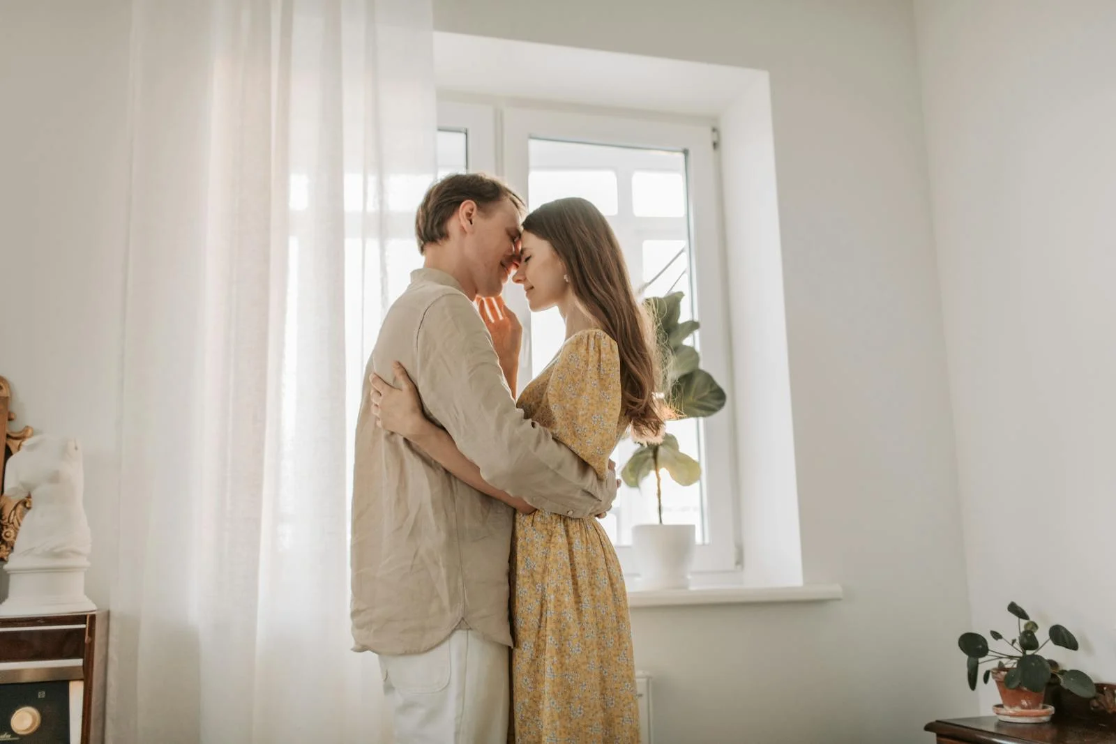 A couple sharing a tender moment indoors surrounded by natural light and plants.