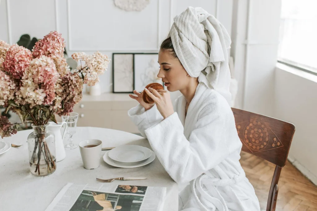 Cozy morning scene with a woman enjoying a croissant and coffee at a dining table indoors.
