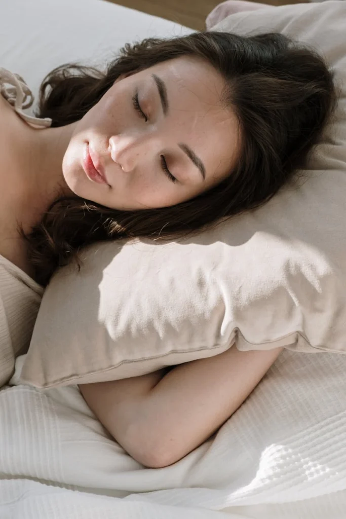 Asian woman sleeping peacefully in morning light with soft linens.