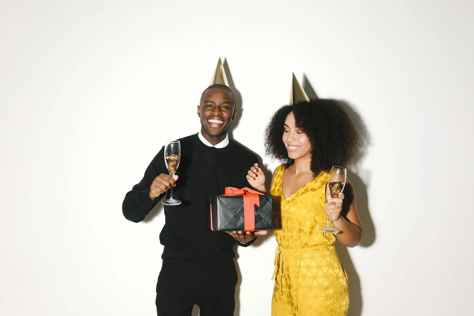 Cheerful couple celebrating indoors with champagne and a gift.