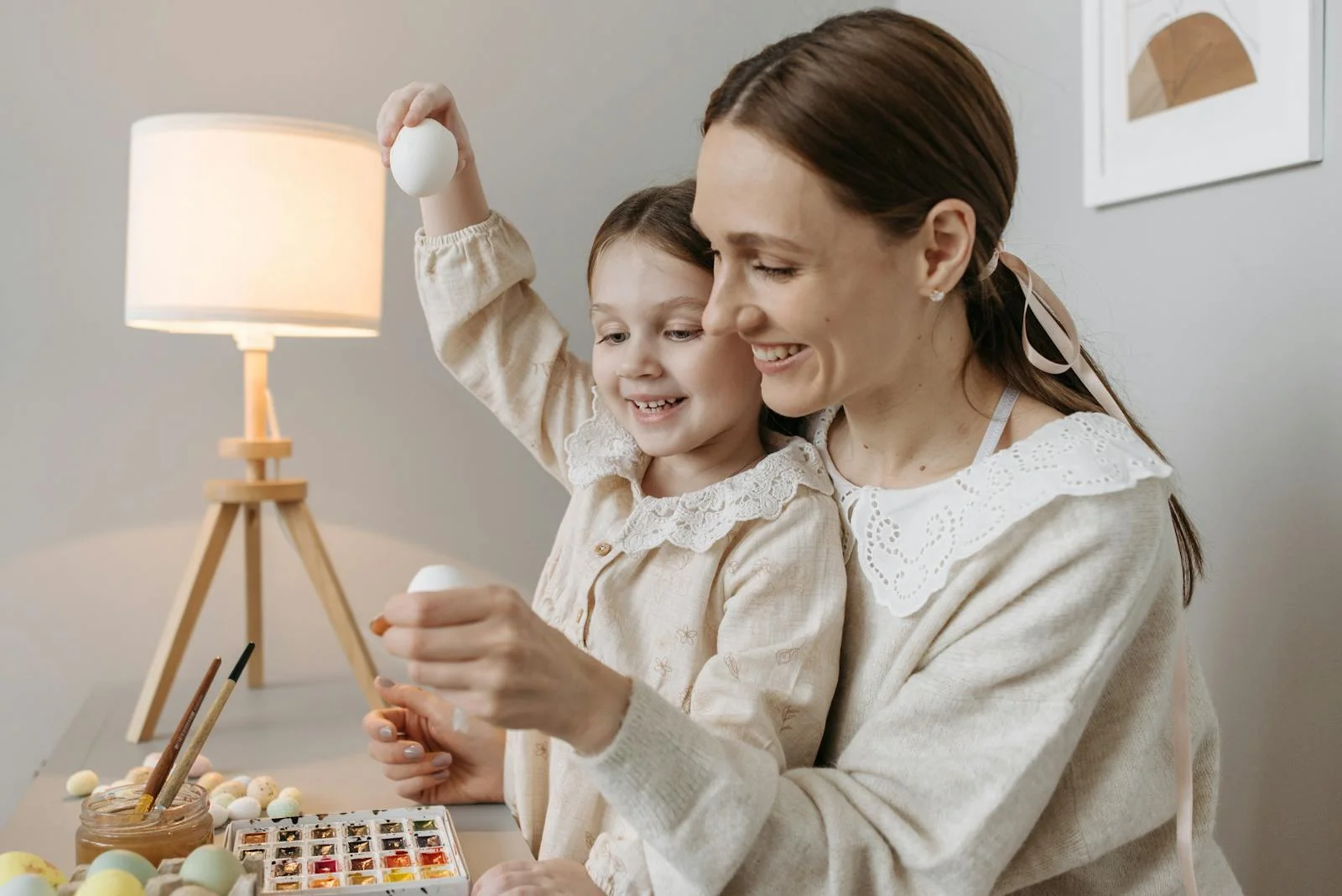 A joyful moment between mother and daughter painting Easter eggs indoors.