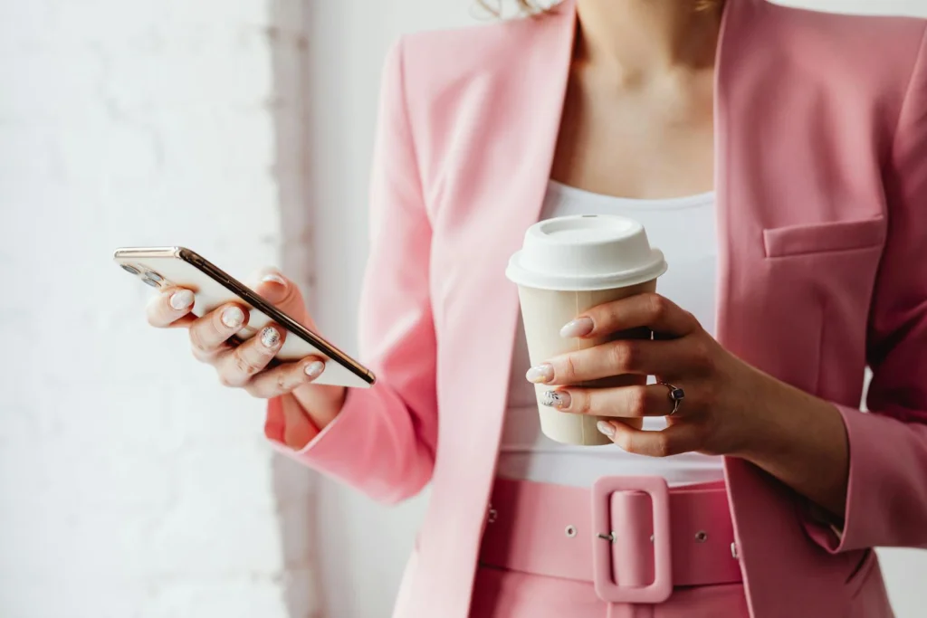 Fashionable woman with coffee cup and phone in a pink suit indoors.