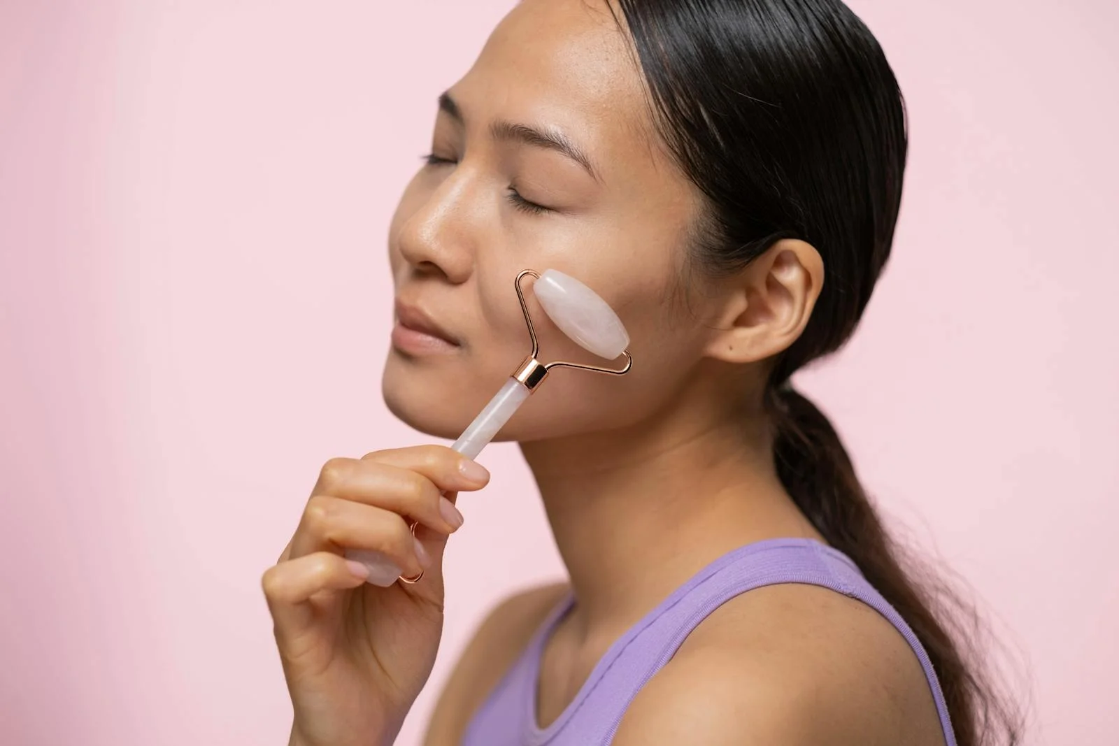 Close-up of a woman using a rose quartz roller on her face for skincare and relaxation.