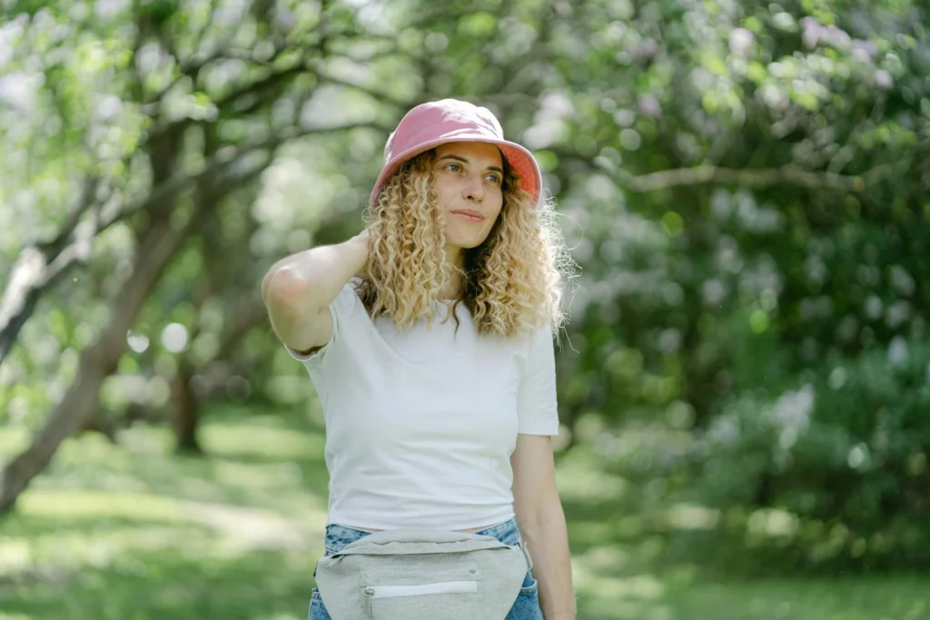 A young woman poses in a serene outdoor setting, wearing a pink hat and casual fashion.