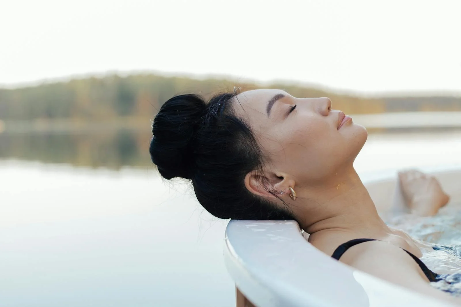 Asian woman enjoying a peaceful moment in an outdoor jacuzzi, eyes closed and content.