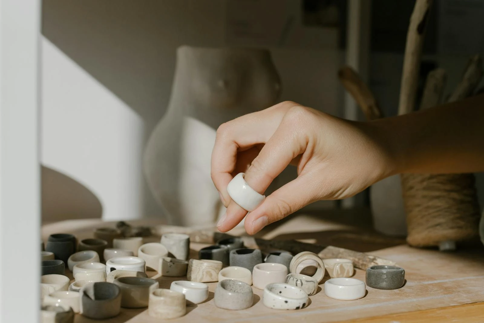 A hand carefully chooses a ceramic ring from a collection in natural light, showcasing detailed craftsmanship.