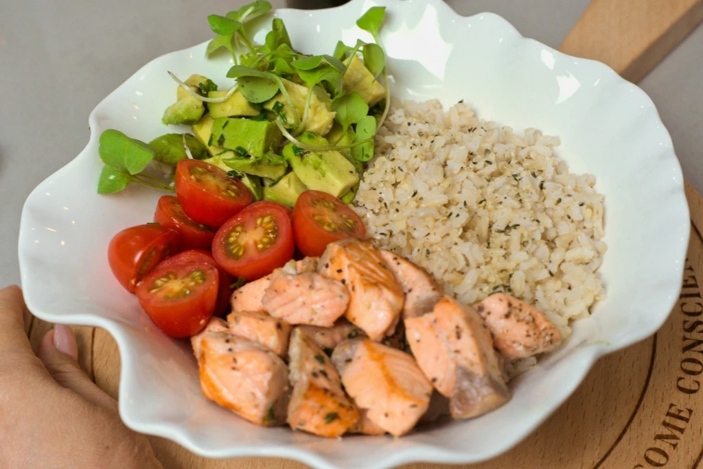 a white bowl filled with chicken, rice, tomatoes and avocado