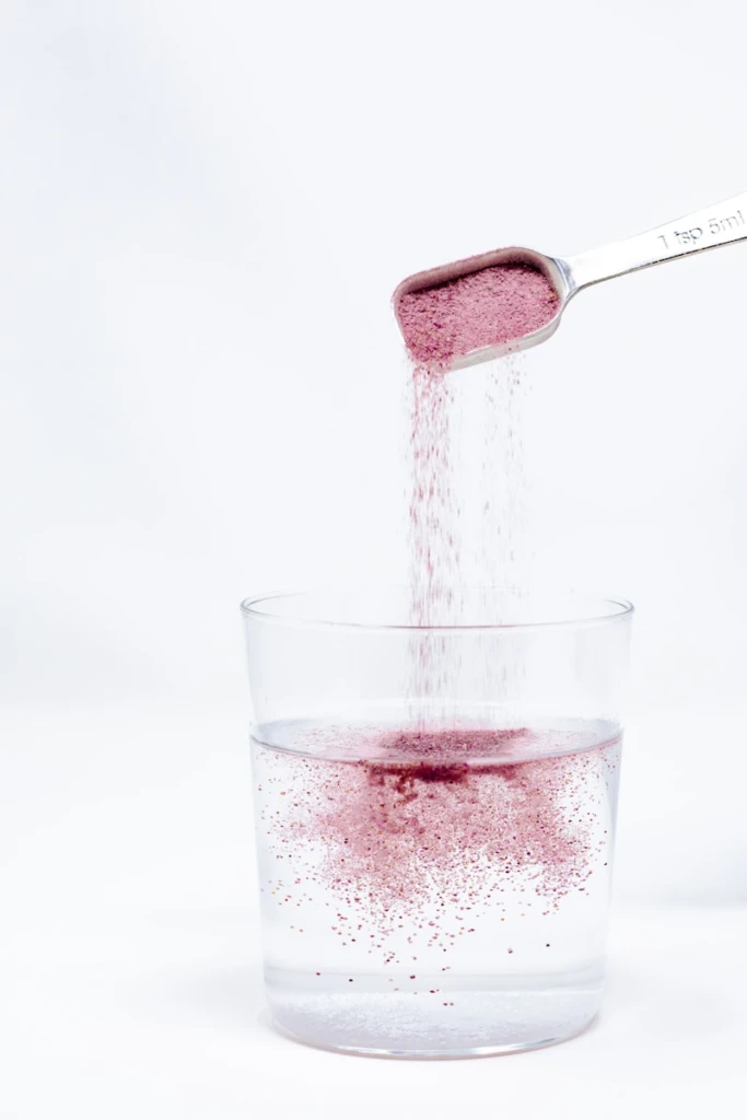 A spoon pouring red liquid into a glass
