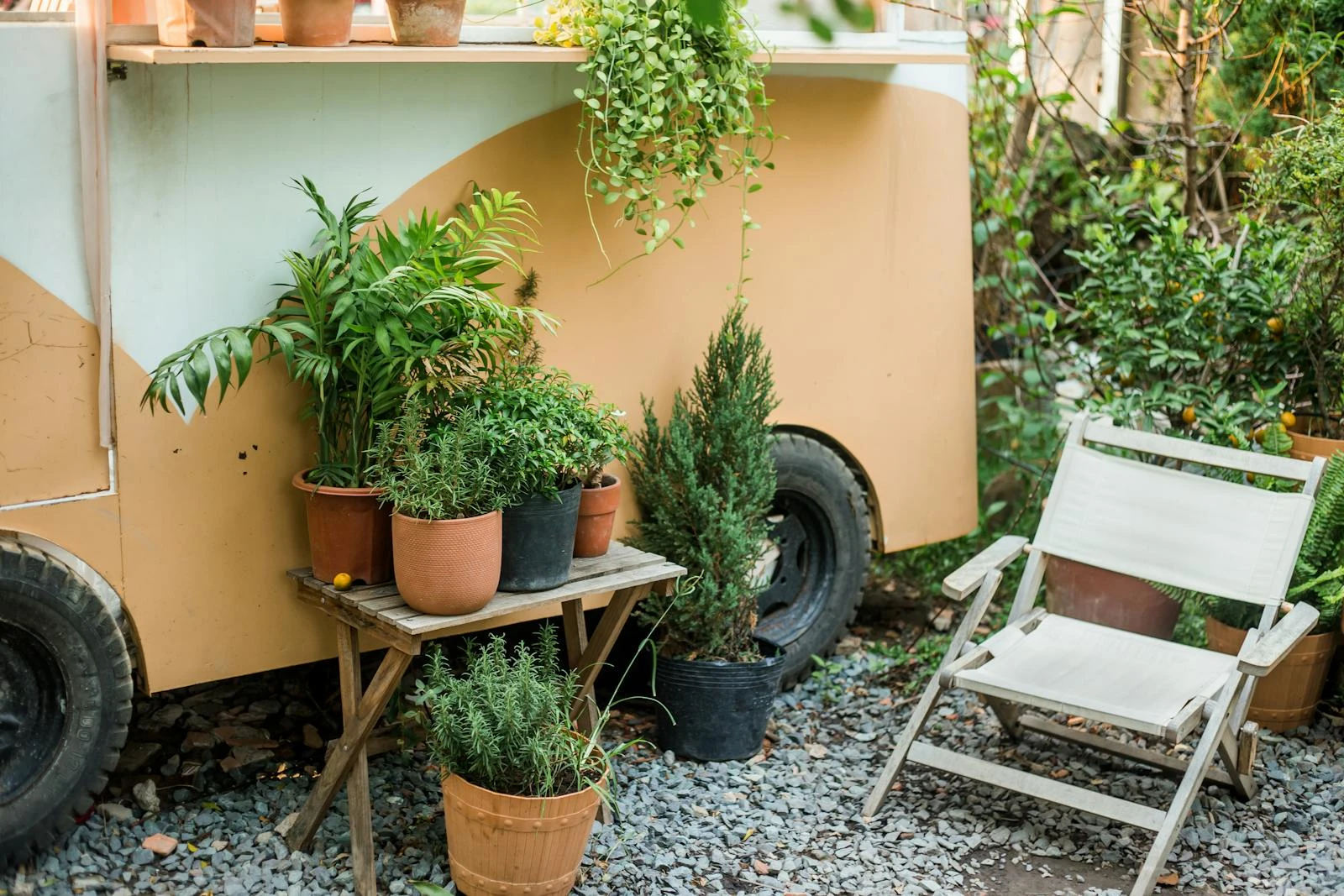 Charming patio space featuring potted plants and a comfortable chair beside a vintage trailer.