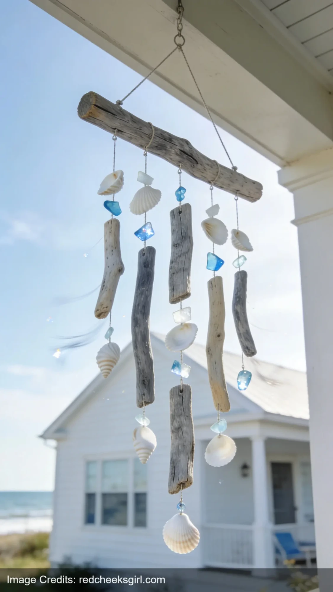 driftwood wind chime with shells and sea glass hanging on coastal porch