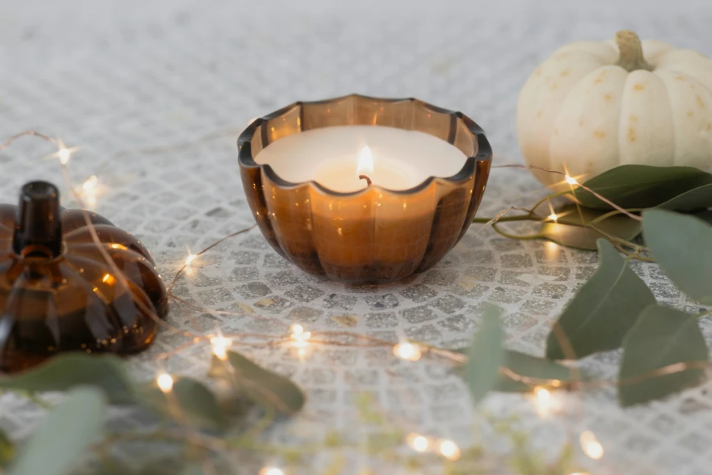 Lit candle in pumpkin-shaped glass with autumn decor.