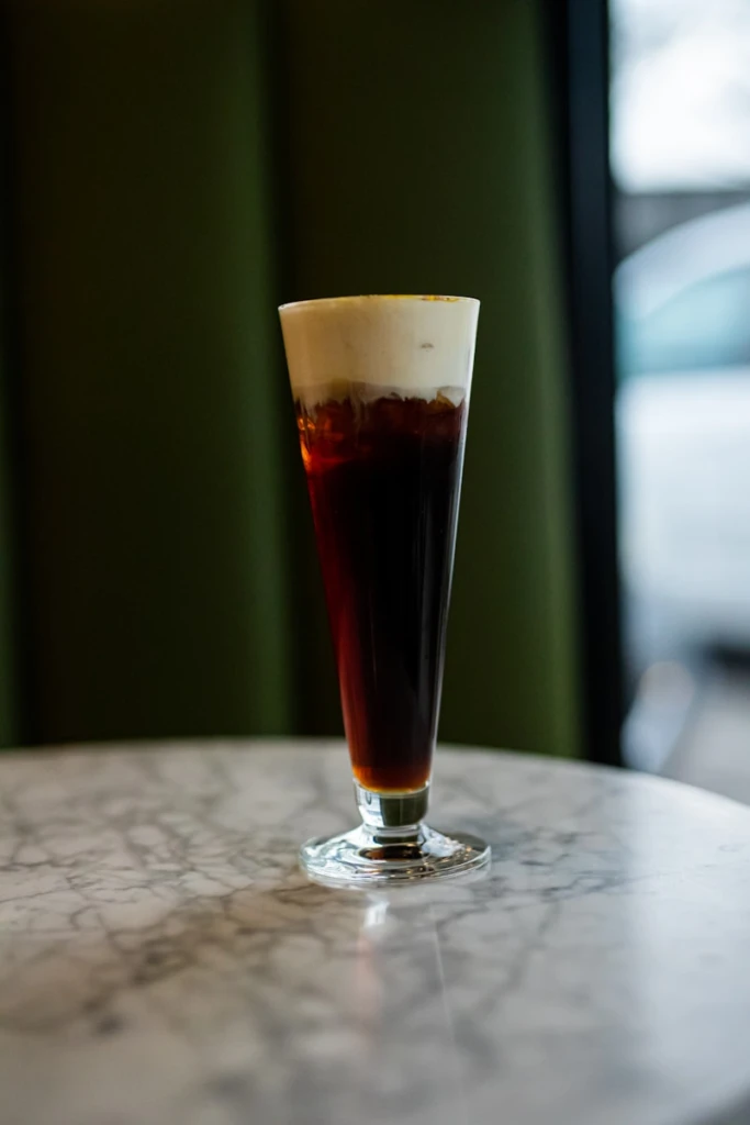 Tall glass of dark coffee with cream