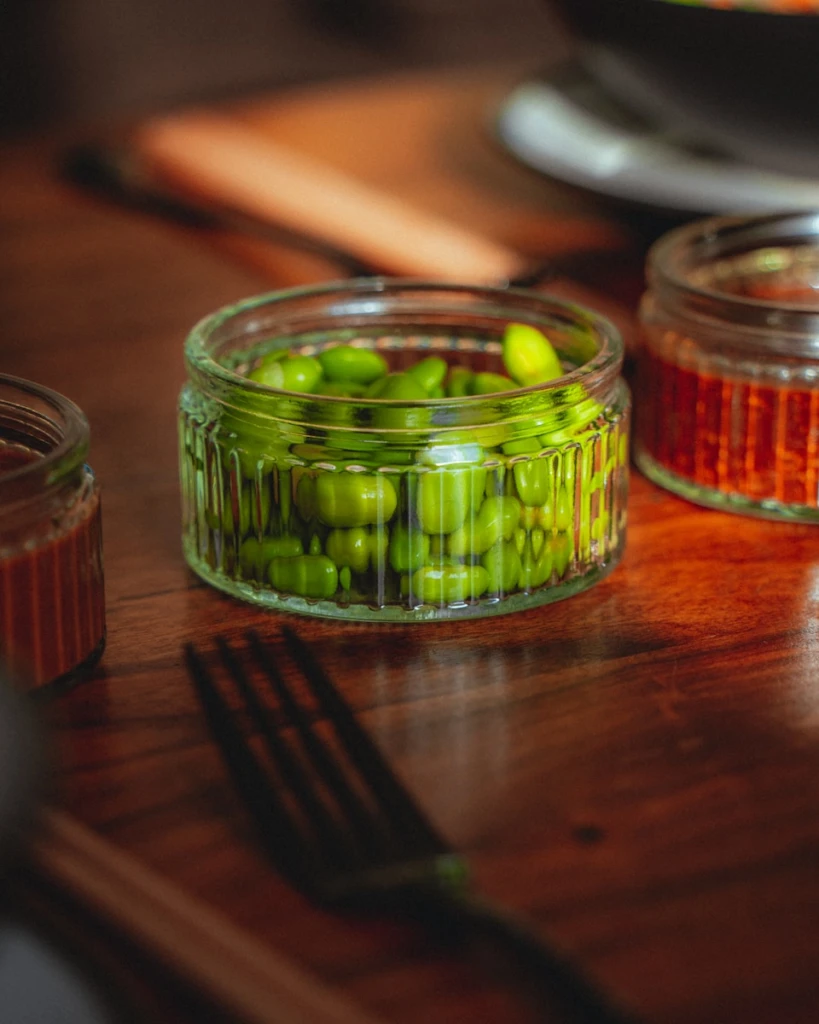 A wooden table topped with jars filled with green beans