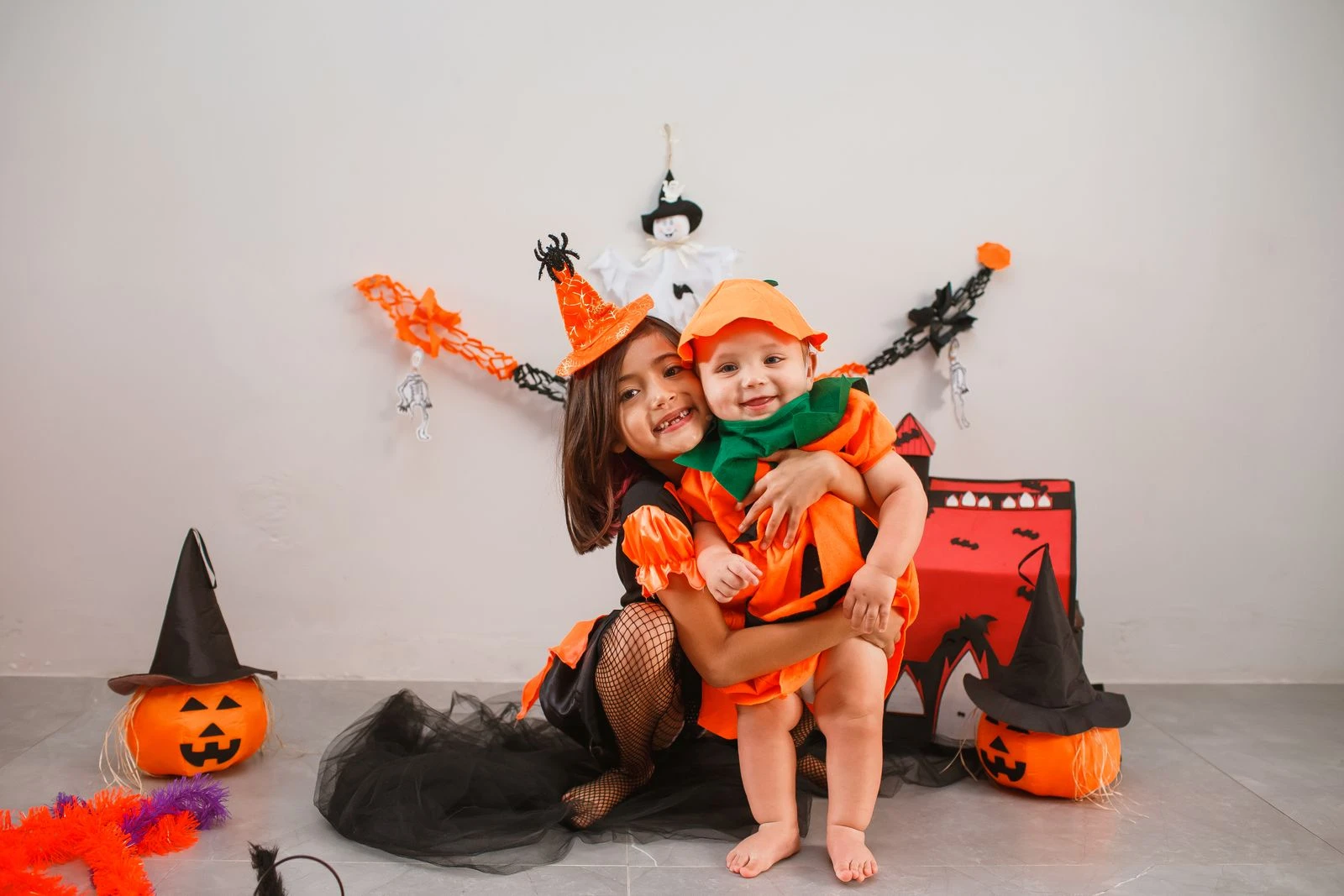Two children dressed as a witch and pumpkin for Halloween, surrounded by festive decorations.
