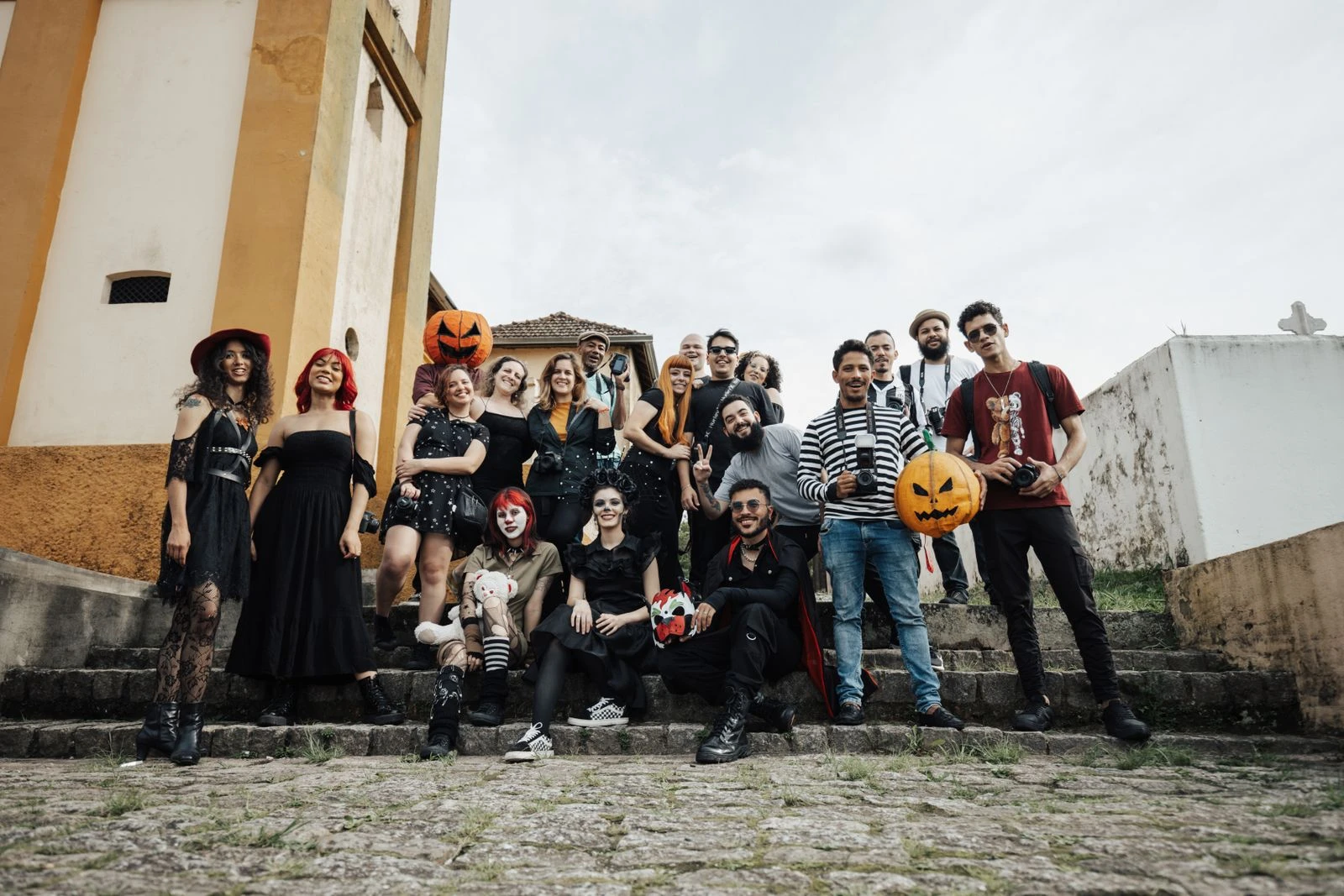 A cheerful group in Halloween costumes with pumpkins on outdoor stone steps.