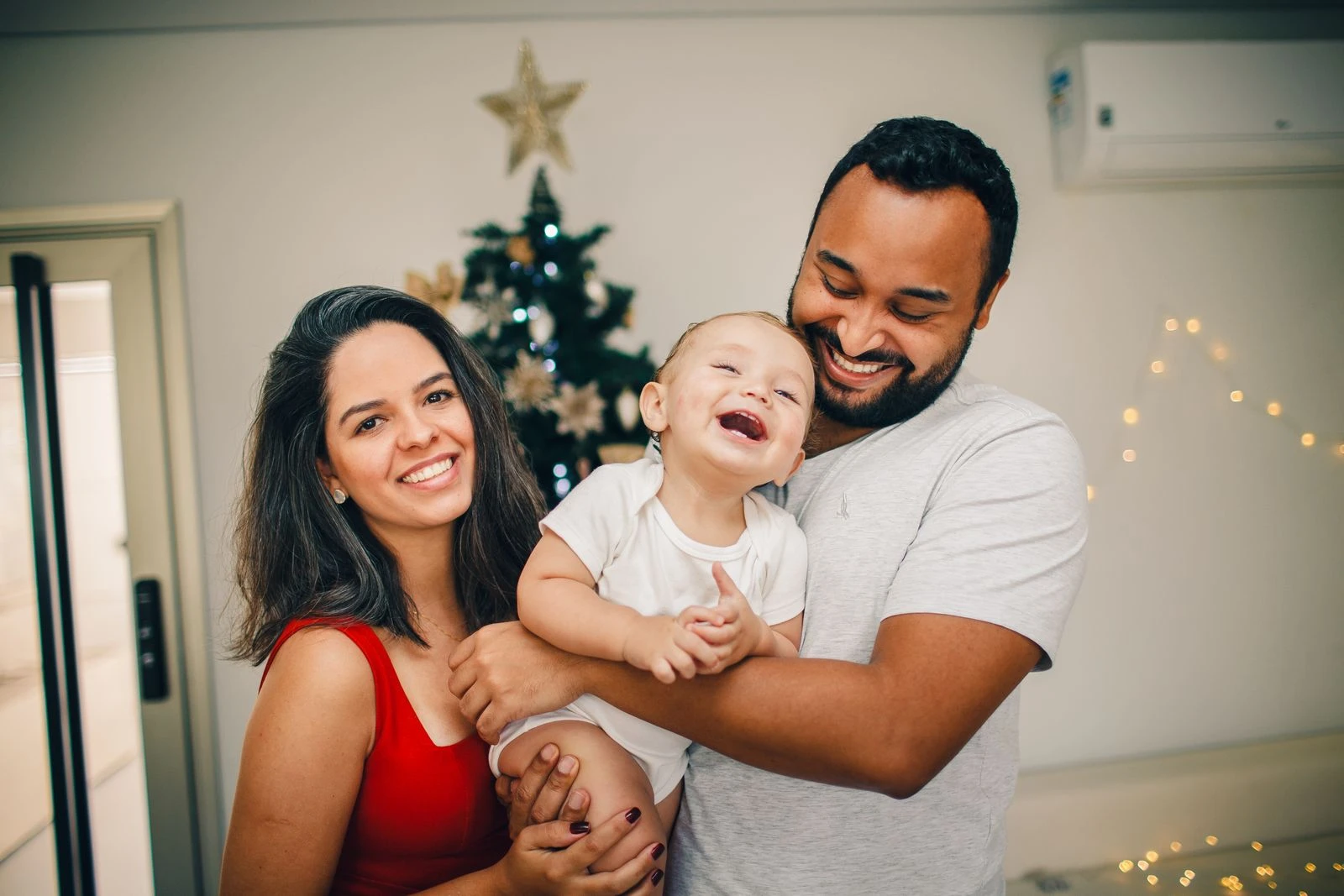 Happy family smiling together by the festive decorated Christmas tree.