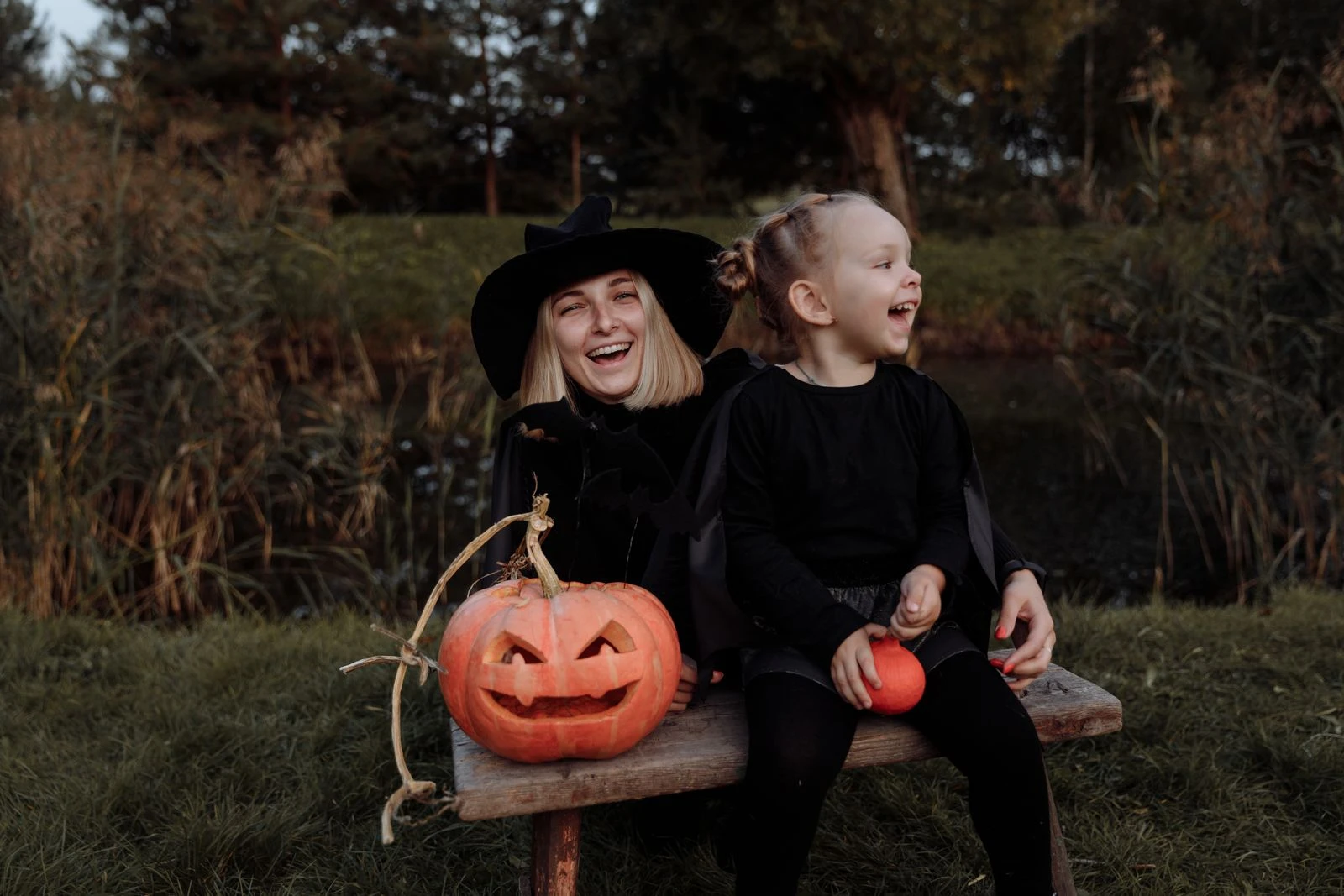 Mother and daughter enjoying Halloween outdoors with pumpkins and witch costumes.