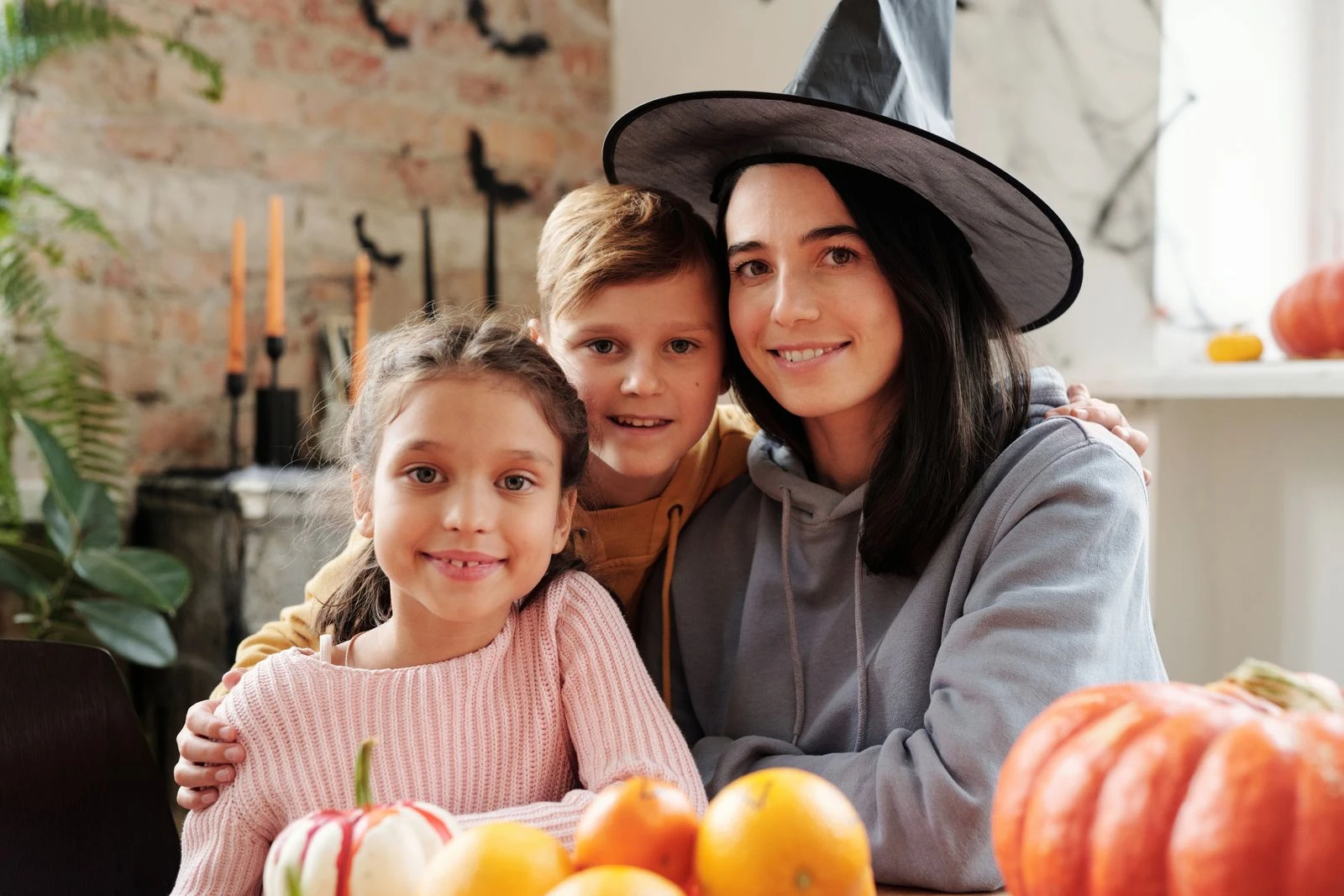 Mother and children celebrating Halloween indoors, surrounded by pumpkins and decorations.