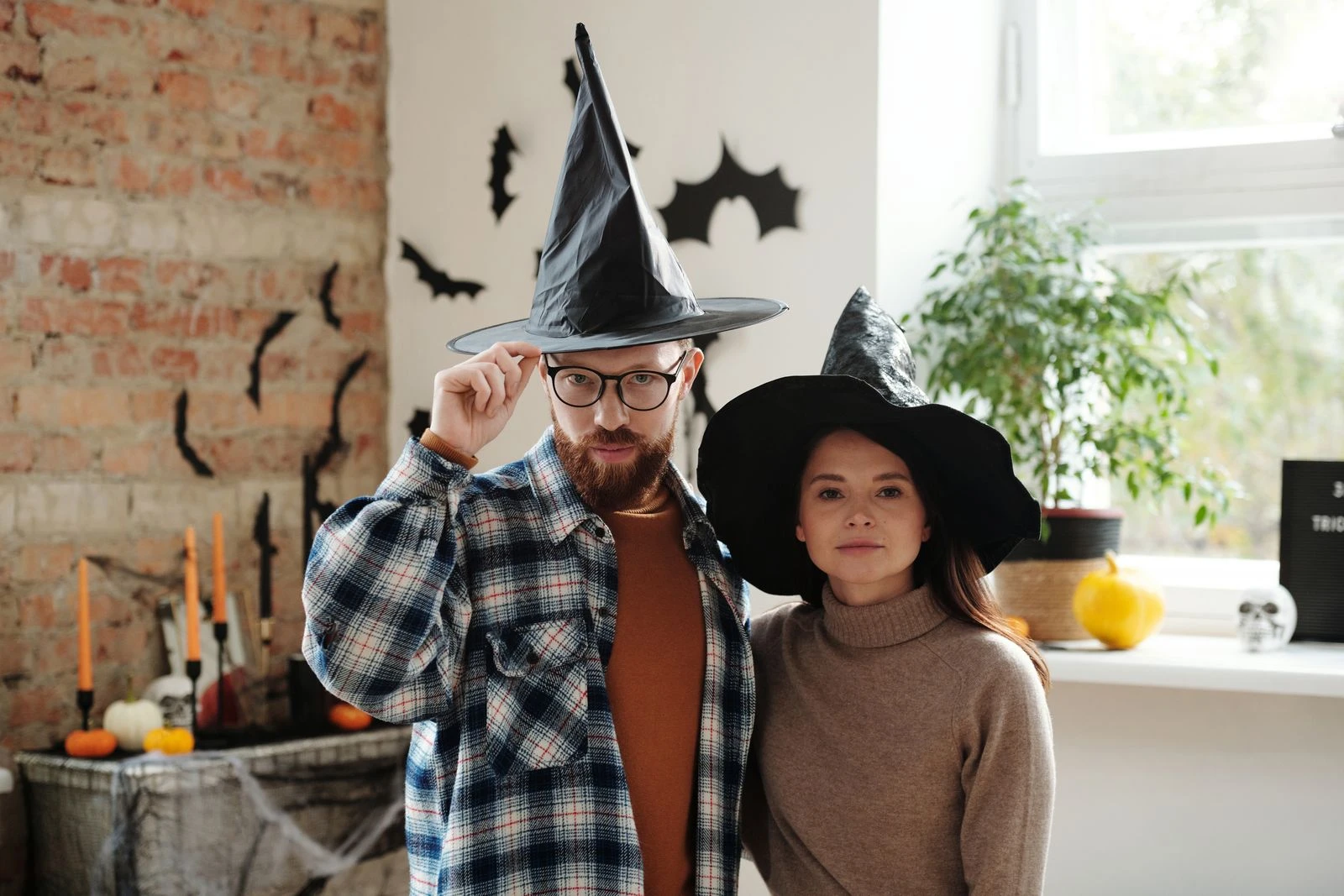 A couple dressed in witch hats enjoying Halloween indoors with festive decor around them.
