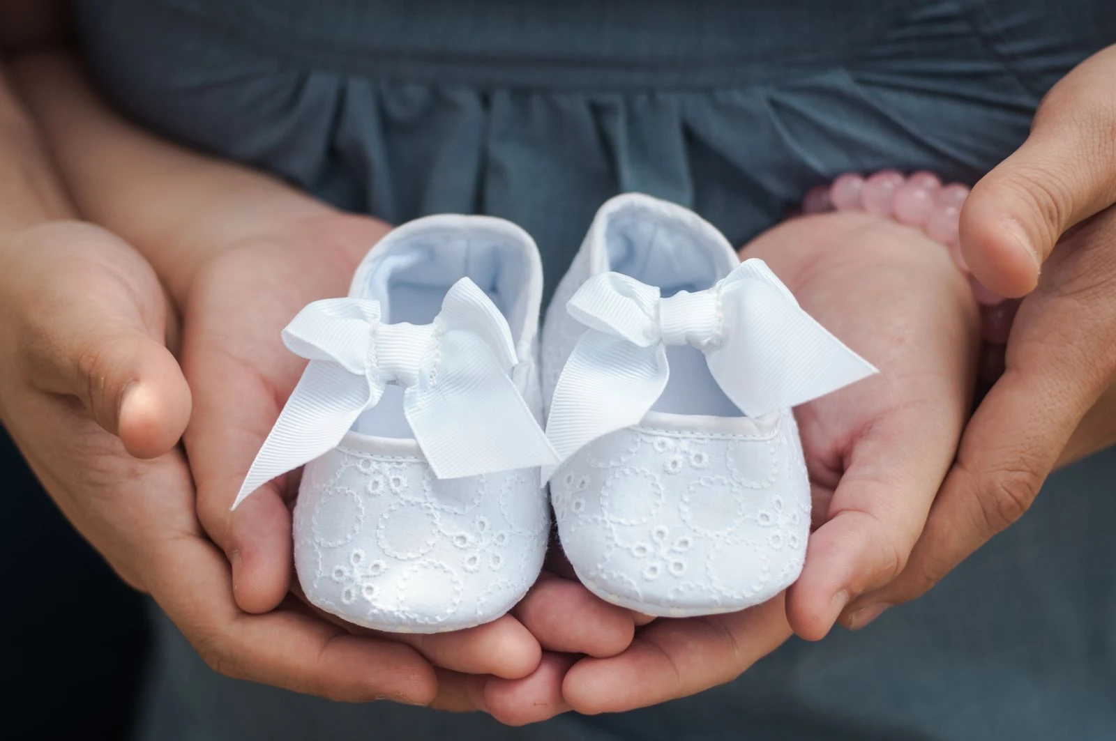 Close-up photo of hands holding white baby shoes with delicate bows, showcasing love and anticipation.