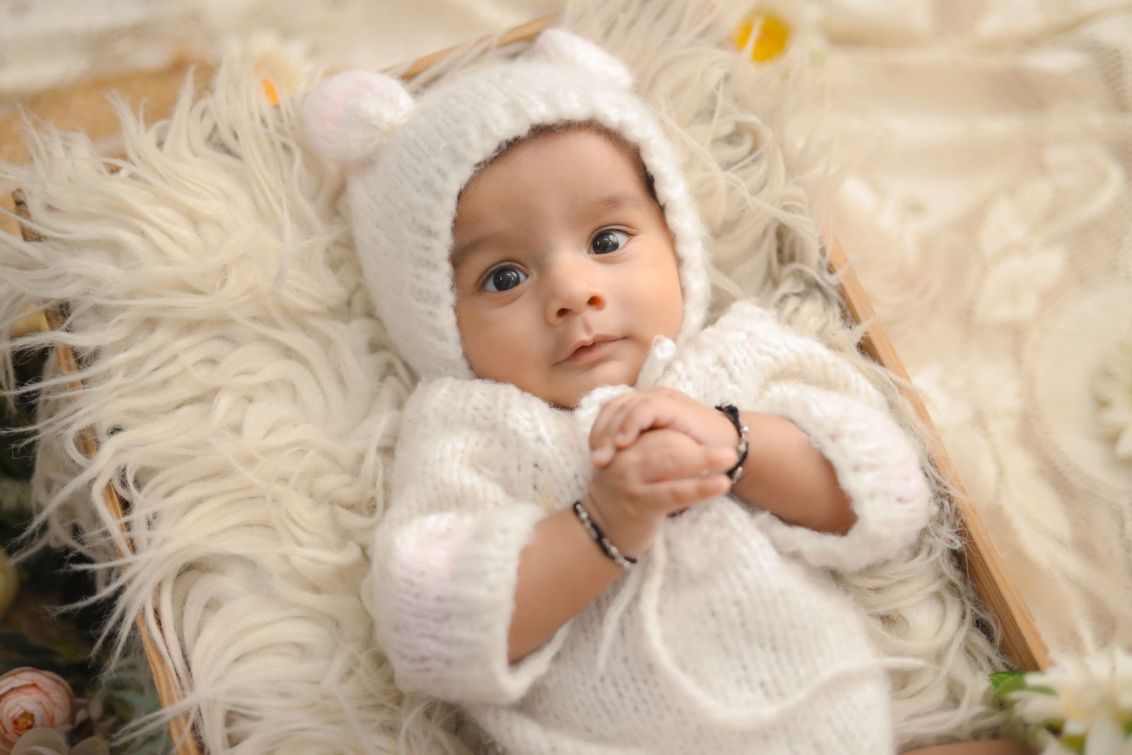 Cute baby wearing a white knitted outfit, lying on soft fur, looking curious and serene.