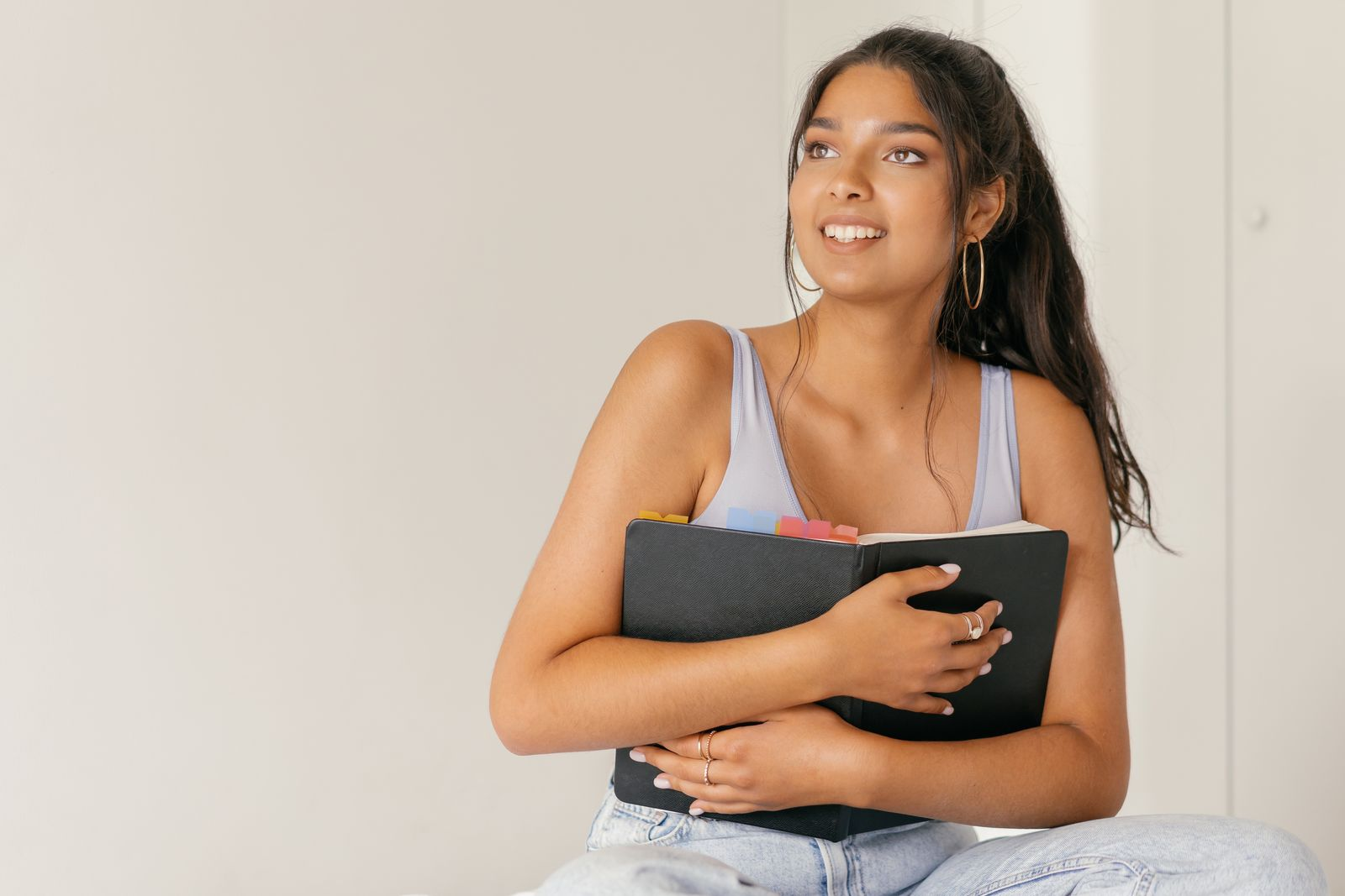 Smiling woman indoors holding a planner, exuding positivity and warmth.