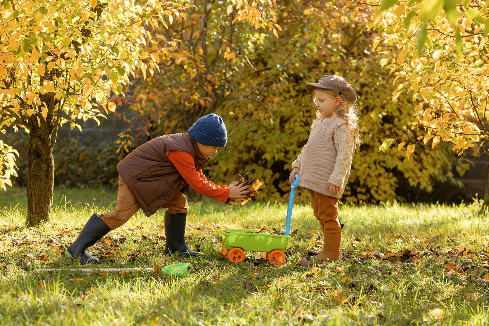 Two kids enjoy a playful autumn day in the garden with a cart and leaves.