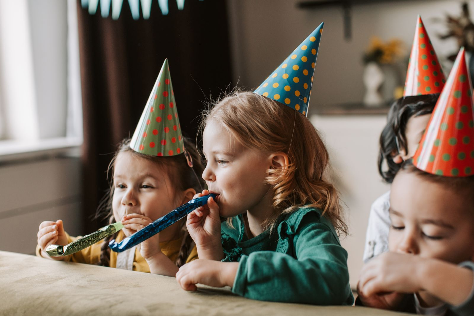 Happy kids with party hats blowing horns at a birthday celebration.