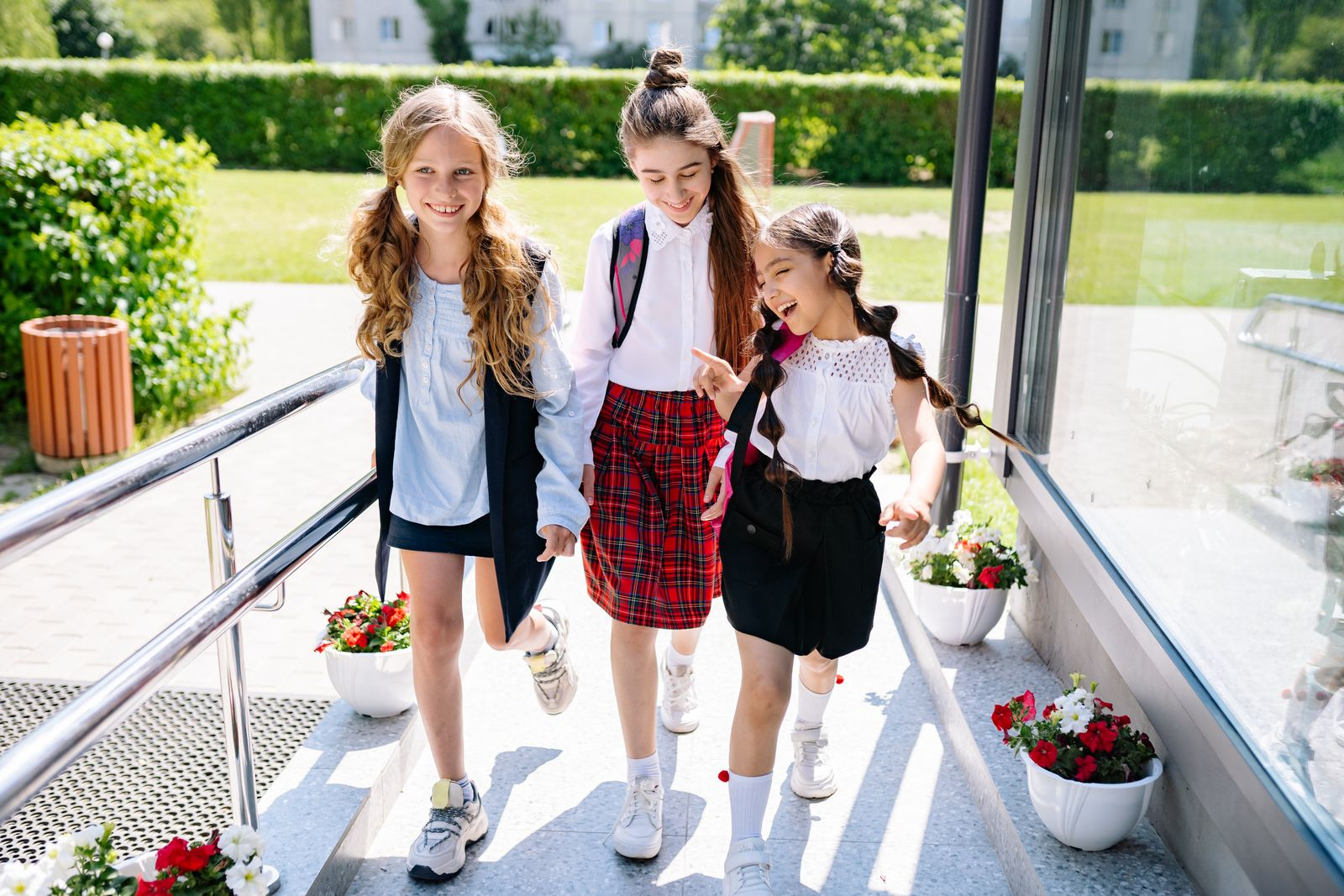 Three cheerful schoolgirls in uniform walking outside, enjoying sunlight and friendship.